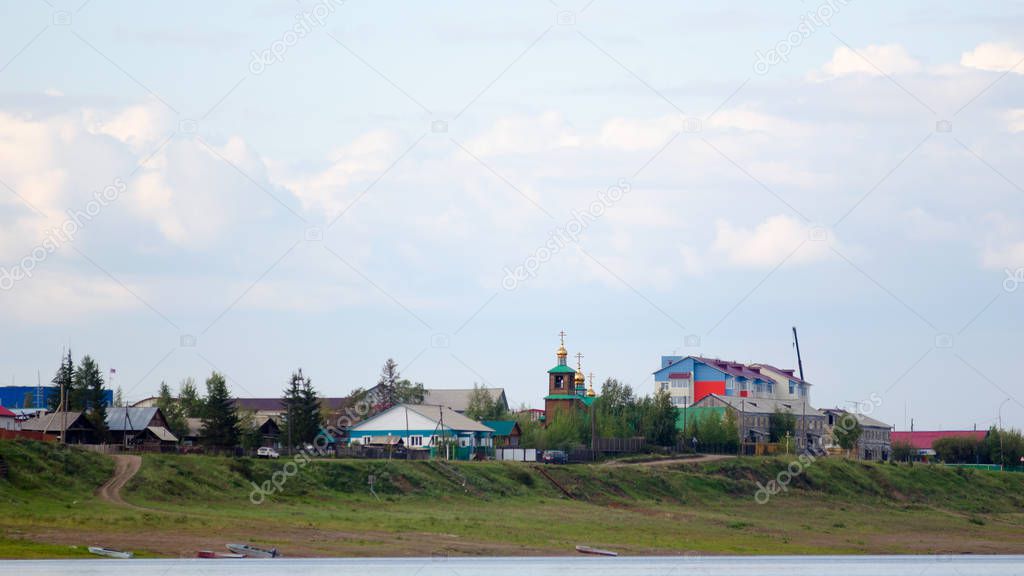 The road from the boats on the river Bank leads to the cliff with houses and silhouettes of cars going to the Church among the houses in the Northern village of ulus Suntar in Yakutia.