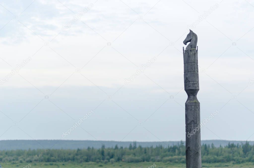 Yakut pole with a horse Serge stands with the head of a horse made of wood on a cliff on the background of endless tundra and forest under the clouds. 