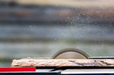 Masaüstünde hızla dönen dairesel testere bıçağı, köy evinin ahşap duvarına karşı her yöne uçan cips ve talaş ile çam tahtasını keser.