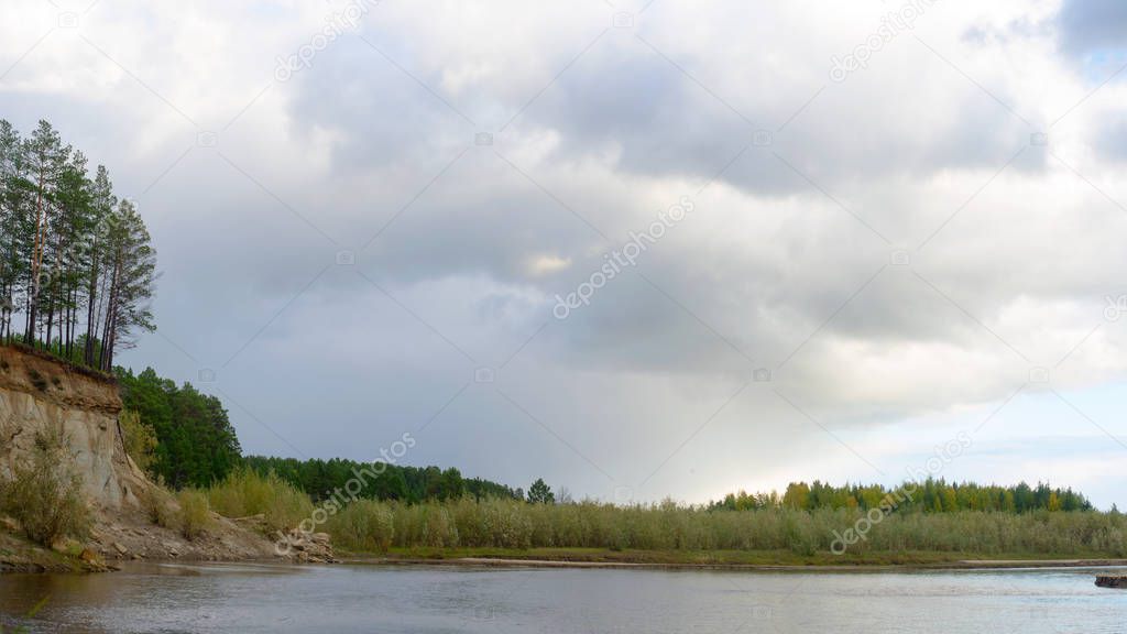 Panorama of the pine forest on a rock on the river Bank with erosion of clay soils and layers of earth under the roots of trees, in the wild tundra of Yakutia, at sunset in the shade of clouds.