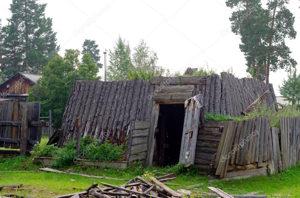 The room for cattle khoton, made of cow dung and wood, overgrown with grass stands with an open door on the grass in the village of Yakutia.