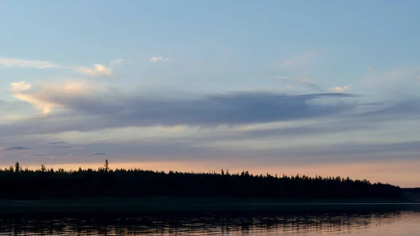 雲と風の波紋とヤクートのスプルースタイガのシルエットと空の下で北川ヴィルイのほとりに明るい青い夕日 — ストック写真