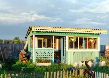 Yakut desenleri ile küçük ev yaz mutfak ulus suntar köyünde parlak akşam tencere asılı çiçekler ile bir köy arsa üzerinde çit arkasında.