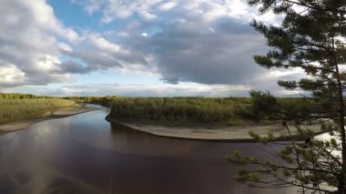 Çim kum ve ağaçlar ile iki kıyısından bir dönüş Yakutia vahşi Kuzey nehrinin akış Video timelapse. Şişman bulutlar sığ su ve kumlu alt gölgeler döküm gökyüzünde çalıştırmak.