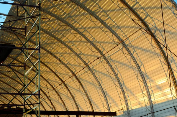 The construction of the roof of the new hangar in a semi-circle of metal with the shadows of the structure at sunset.