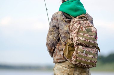 Yol taktik sırt çantası boyama Yakut kız-turist fenerinin arkasına giyilen gökyüzü ve bulutlar ve köknar taiga arka planda Vilyui nehri Kıyısında şapka bir balık yakalar.