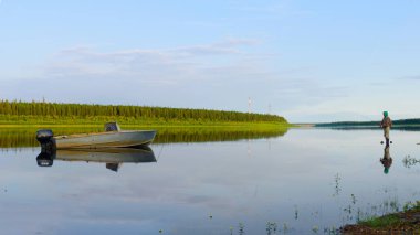Bir sırt çantası fener balıkçılık ile Yakut kız turist ve tekne ve motor yanında Rusya ladin ormanlarıtuntdra vahşi Kuzey nehri vilyu üzerinde dönen yem atar.