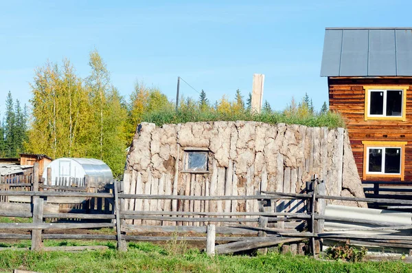The room for cattle hoton, made of cow dung and wood, overgrown with grass stands on a modern plot with a house in the North of Yakutia.
