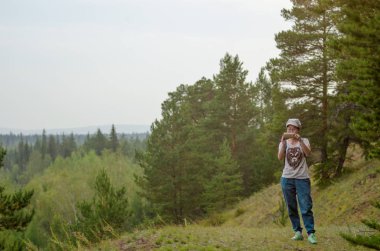 Yakut Asyalı kız turist ufukta orman ile Kuzey Yakutistan ladin ormanında dağdan telefon görünümünde fotoğraf çeker.
