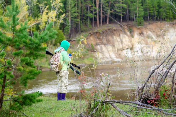 The girl tourist with backpack and fishing rods in their cases standing on the banks of a wild u-turn North of the river taking your phone to see the way forward in the Northern taiga of Yakutia.