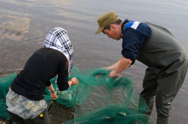 Bir adam ile birlikte bir şal ve manikür zarif bir Yakut kız geleneksel Kuzey Yakut balıkçılık üzerinde nehrin su yakınında bir balık ağı balık seçin.