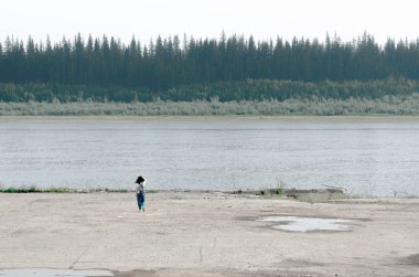 Sırt çantası ile Kız gezgin ladin ormanları ve diğer tarafta Yakutia tundra ile nehrin kuzey eski iskelekuzey kıyısında saç dokunmadan beton kaldırım kenarına gider.