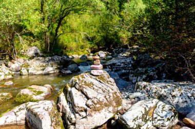 Düz yuvarlak taşlardan oluşan bir piramit ormanda gün boyunca Altay bir dağ hızlı nehrin ortasında büyük bir taş üzerinde duruyor.