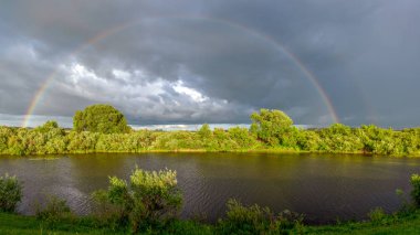 Parlak bir günde, küçük bir nehrin üzerindeki yağmurda iki büyük gökkuşağı manzarası.. 