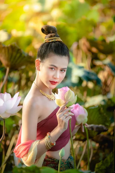 Asyalı kadın nilüfer çiçeği topluyor ve geleneksel Tayland elbiseleri giyiyor.