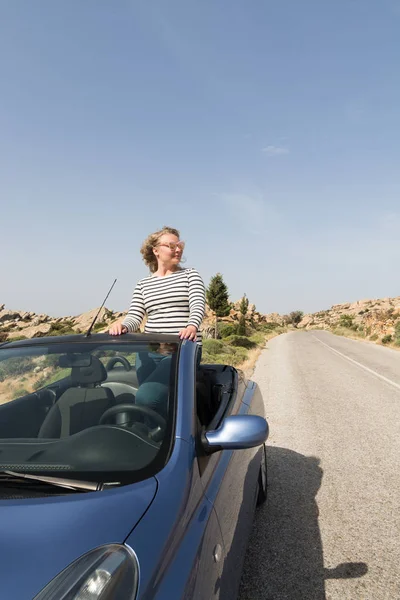 Jovem mulher loira dirigindo em carro de aluguel azul conversível sem telhado na estrada da montanha na ilha de Naxos, Grécia — Fotografia de Stock