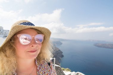 Sarışın genç kadın bir hasır şapkalı, Santorini Island, Yunanistan bardaklarda Oia Köyü yansıması. Atış, geniş açı objektif odak yansıması