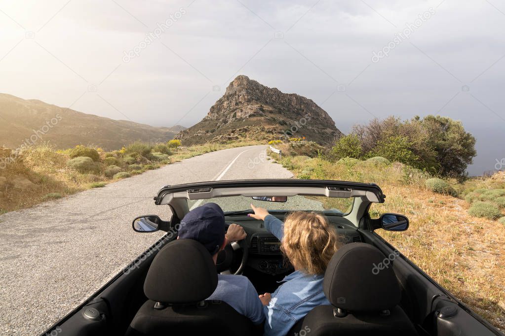 Young couple driving in convertible blue car without roof on mountain road in Naxos island, Greece. Wide angle lens shot.