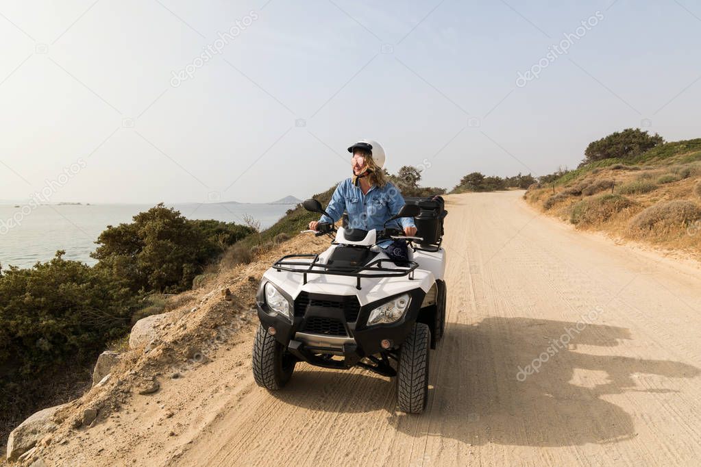 Young woman driving rental quad bike on seaside road in Naxos island, Greece