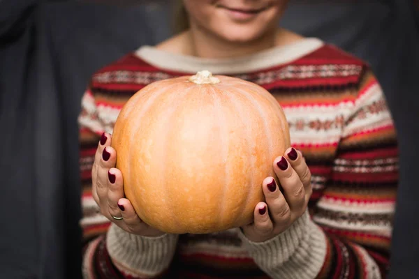 Young smiling woman in authentic sweater holding a pumpkin in her hands