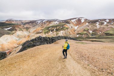 Kadın sarı yağmurluk yokuş yukarı Landmannalaugar Milli Parkı, İzlanda renkli dağlarında hiking.