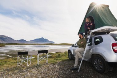 Hofn, İzlanda - Ağustos 2018: Çadır çatı ile merdiven offroad araba yanında oturan genç çift.