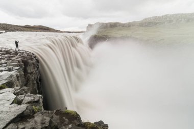 İnsan figürü ayakta Vatnayokull Milli Parkı, İzlanda Dettifoss şelale yanındaki uçurumun kenarında. Bulutlu gün, uzun pozlama.