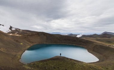 İnsan figürü ayakta su Krafla yanardağ, İzlanda krater dolu. Panoramik çekim, bulutlu gün.