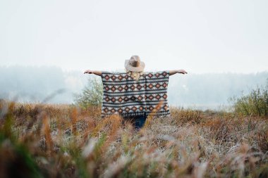 Şapka ve yüksek kahverengi çim otantik panço ayakta Sisli sabah çapında ekledi kadında hissettim.