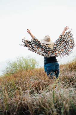 Geniş ekledi kadında şapka ve yüksek kahverengi çim otantik panço ayakta Sisli sabah hissettim. Dikey yönlendirme.