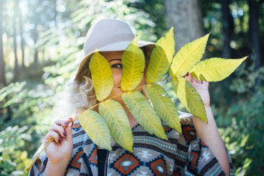 Geniş ekledi kadın yüzü büyük ağaç yaprak arkasında saklanıyor otantik panço ve şapka hissettim.
