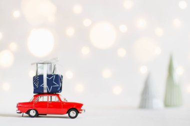 Red toy car with a christmas presents on the roof, garland bokeh on the background, shallow depth of field. clipart