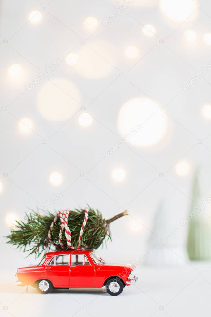 Red toy car with a christmas tree on the roof, garland bokeh on the background, shallow depth of field, vertical orientation.