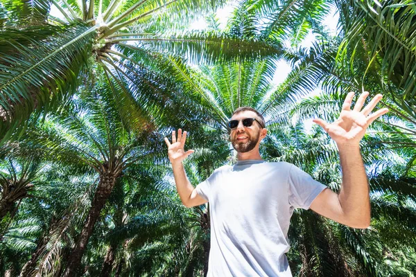 Bebaarde lachende man met glazen staande in het palmboom woud — Stockfoto