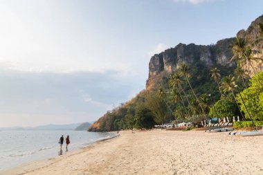 Tayland 'ın Krabi eyaletinde gün batımında Pai Plong sahilinde yürüyen genç bir çift.