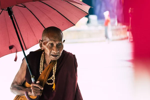 Yangon, myanmar - märz 2019: alter buddhistischer mönch mit rotem schirm spaziert in der shwedagon-pagode — Stockfoto