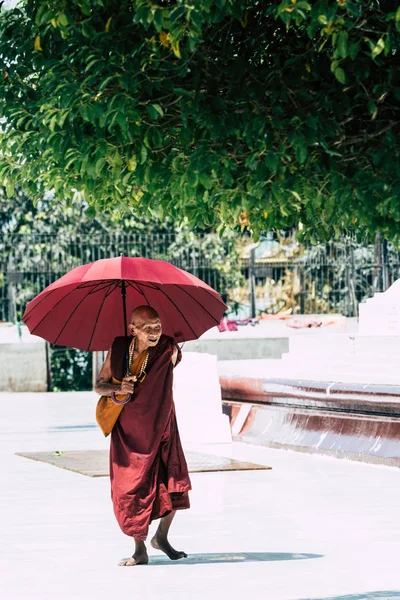 Yangon, myanmar - märz 2019: alter buddhistischer mönch mit rotem schirm spaziert in der shwedagon-pagode — Stockfoto