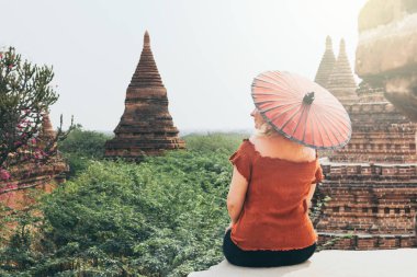Myanmar'da pagodalara ve antik Bagan tapınaklarına bakan kırmızı şemsiyeli kadın