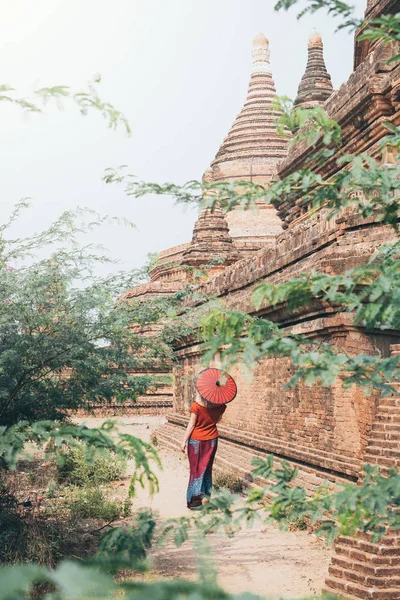 Mulher branca loira com guarda-chuva vermelho está entre templos e pagodes da antiga Bagan em Mianmar — Fotografia de Stock