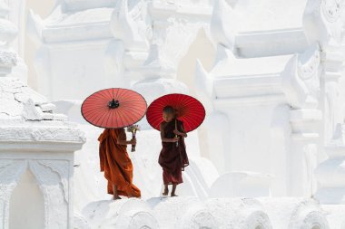 Mandalay, Myanmar - Nisan 2019: Myatheindan Pagoda'nın duvarlarında yürüyen kırmızı şemsiyeli Budist acemi rahipler