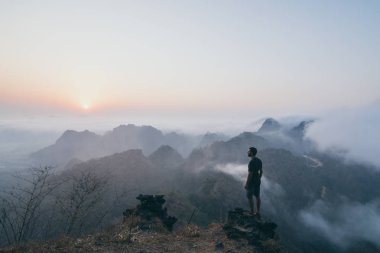 Hpa-an, Myanmar gün doğumunda sisli sabah tropikal dağlara bakan kaya üzerinde duran adam