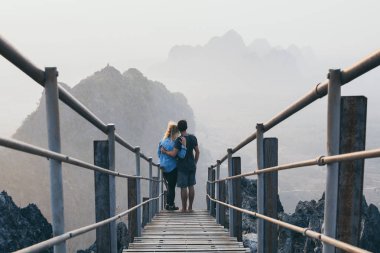 Young couple standing on mountain peak with stairs going down during sunrise foggy morning in Hpa-An, Myanmar clipart