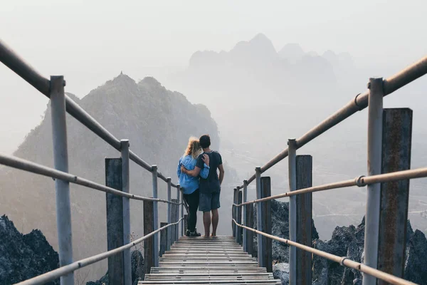 Pareja joven parada en el pico de la montaña con escaleras bajando durante la mañana brumosa amanecer en Hpa-An, Myanmar — Foto de Stock