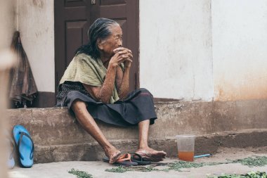 Luang Prabang, Laos-Mayıs 2019: eski Lao kadın ev verandasında oturur, düşünceli bir görünüm