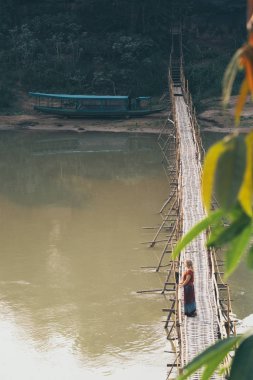 Luang Prabang şehir, Laos Nam Ou nehri üzerinde geleneksel mevsimsel bambu köprü üzerinde kırmızı ayakta kırmızı giyinmiş genç Kafkas kadın