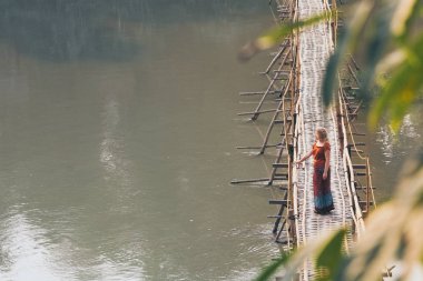 Luang Prabang şehir, Laos Nam Ou nehri üzerinde geleneksel mevsimsel bambu köprü üzerinde kırmızı ayakta kırmızı giyinmiş genç Kafkas kadın