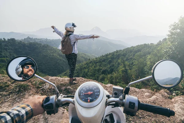 Laos dağlarında motosikletsüren beyaz bir çift. Kadın uçurumun kenarında duruyor, eller yukarı. Nong Khiaw köyü, Laos