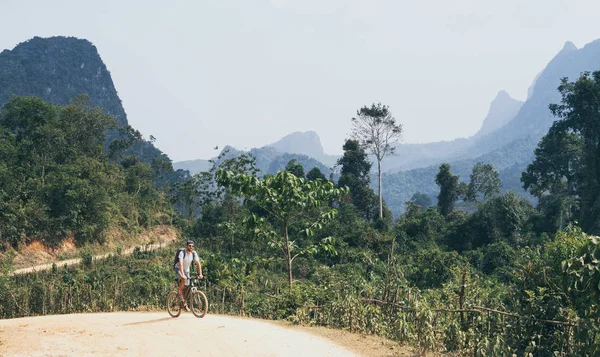 Jonge Kaukasische man rijden een mountainbike bergopwaarts in Muang Ngoi Village, Laos — Stockfoto