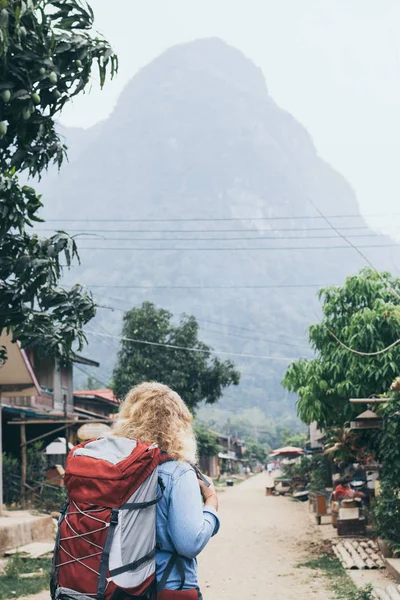 Jeune femme blonde caucasienne avec sac à dos debout sur la rue centrale du village de Muang Ngoi, Laos — Photo