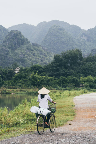 Ninh Binh, Vietnam - May 2019: Vietnamese woman in rice conical hat rides bicycle in Tam Coc national park Royalty Free Stock Images